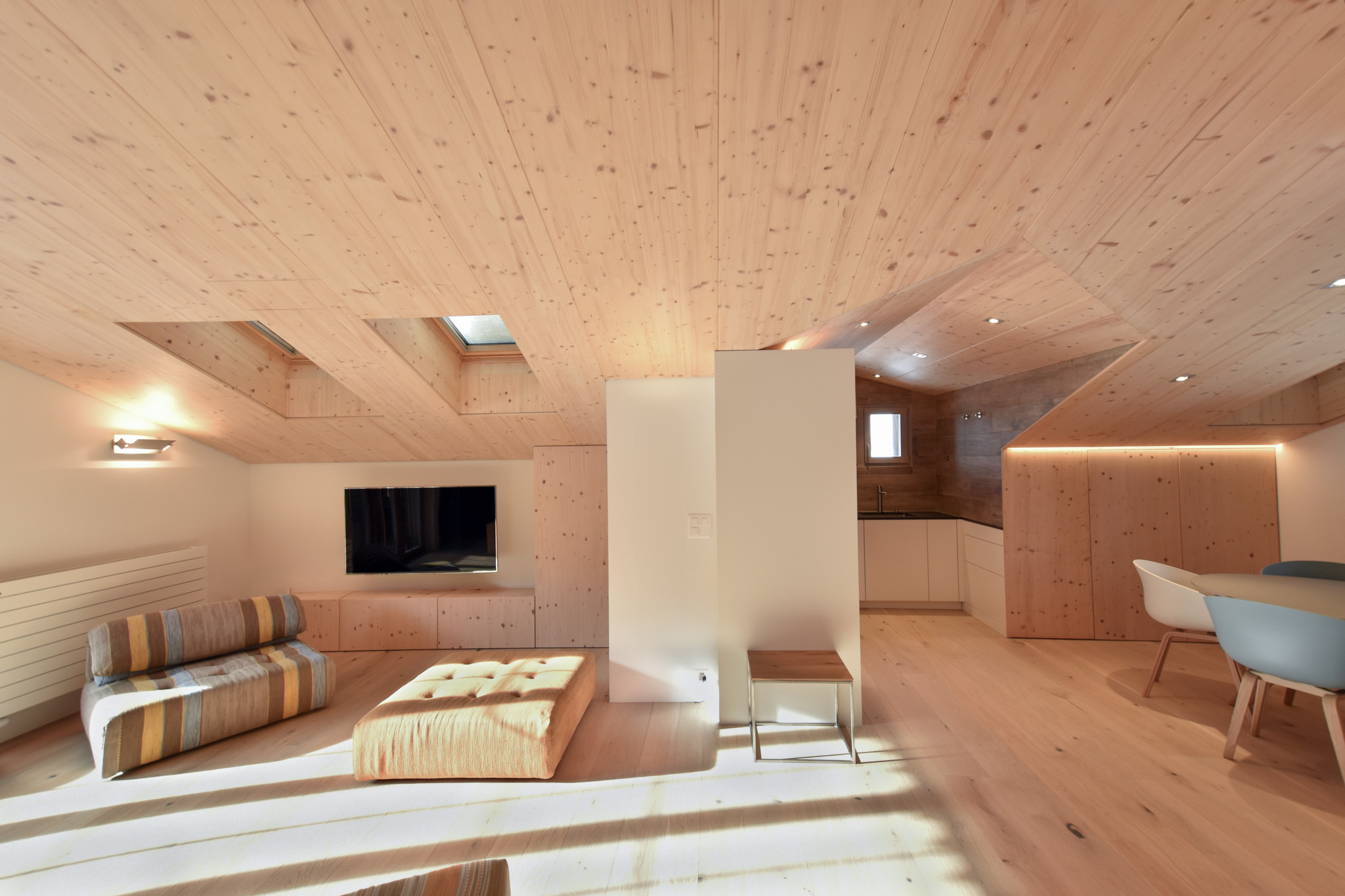 A stylish, bright loft with wooden walls, a cozy seating area, and a kitchen, illuminated by natural light from skylights.
