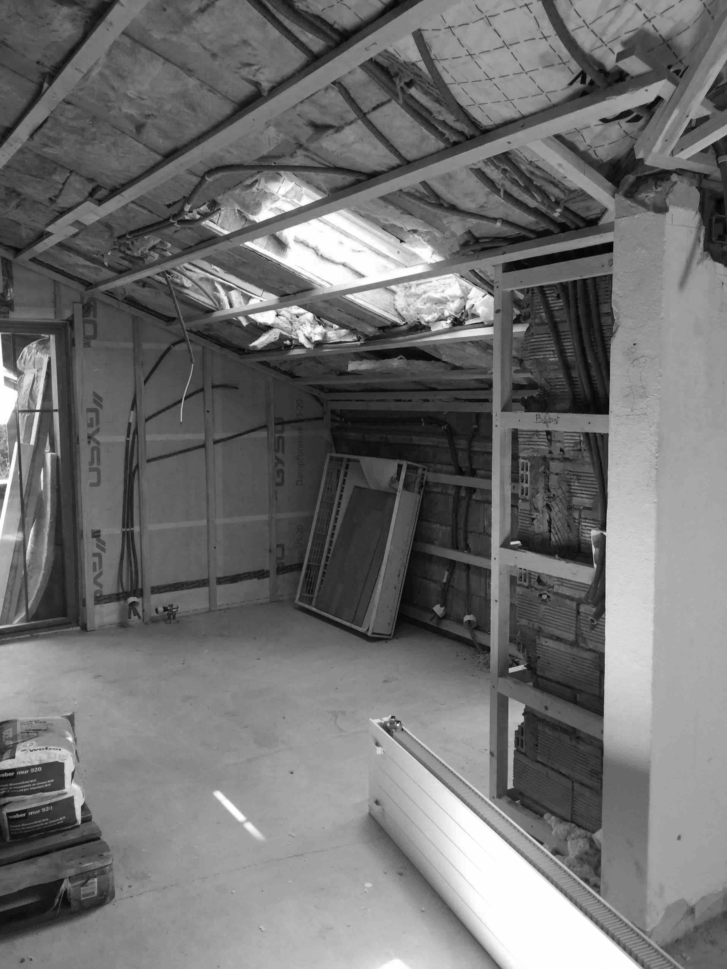A partially constructed room with exposed beams, insulation, and electrical wiring; tools and materials scattered on the floor.