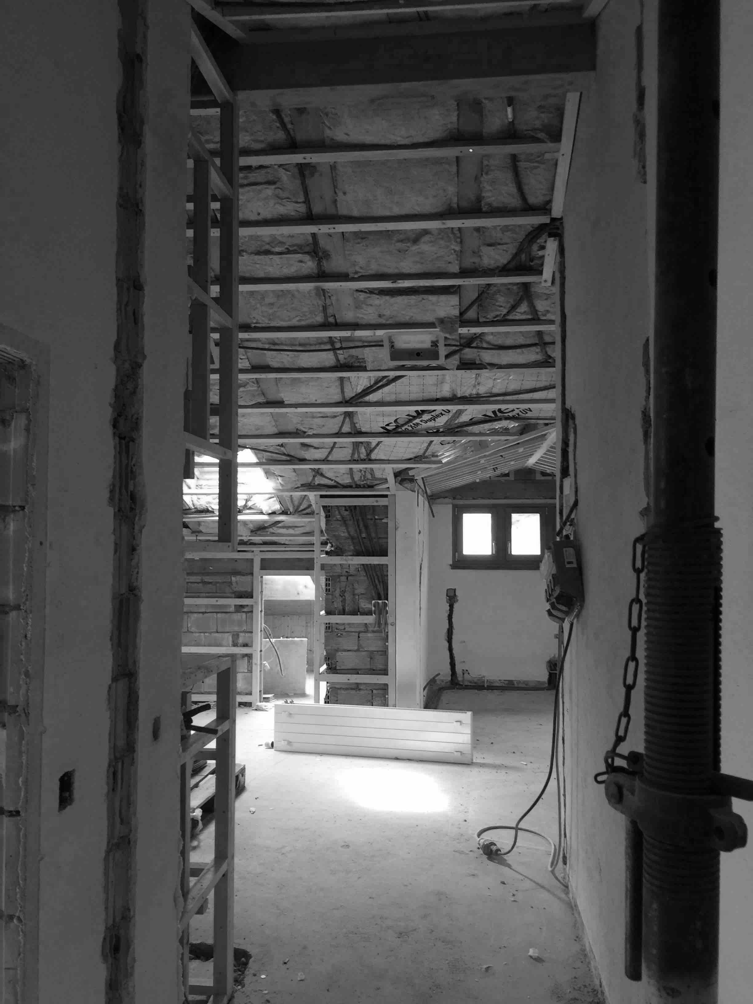 Interior of a partially constructed building featuring exposed beams, construction materials, and a beam of light illuminating the floor.