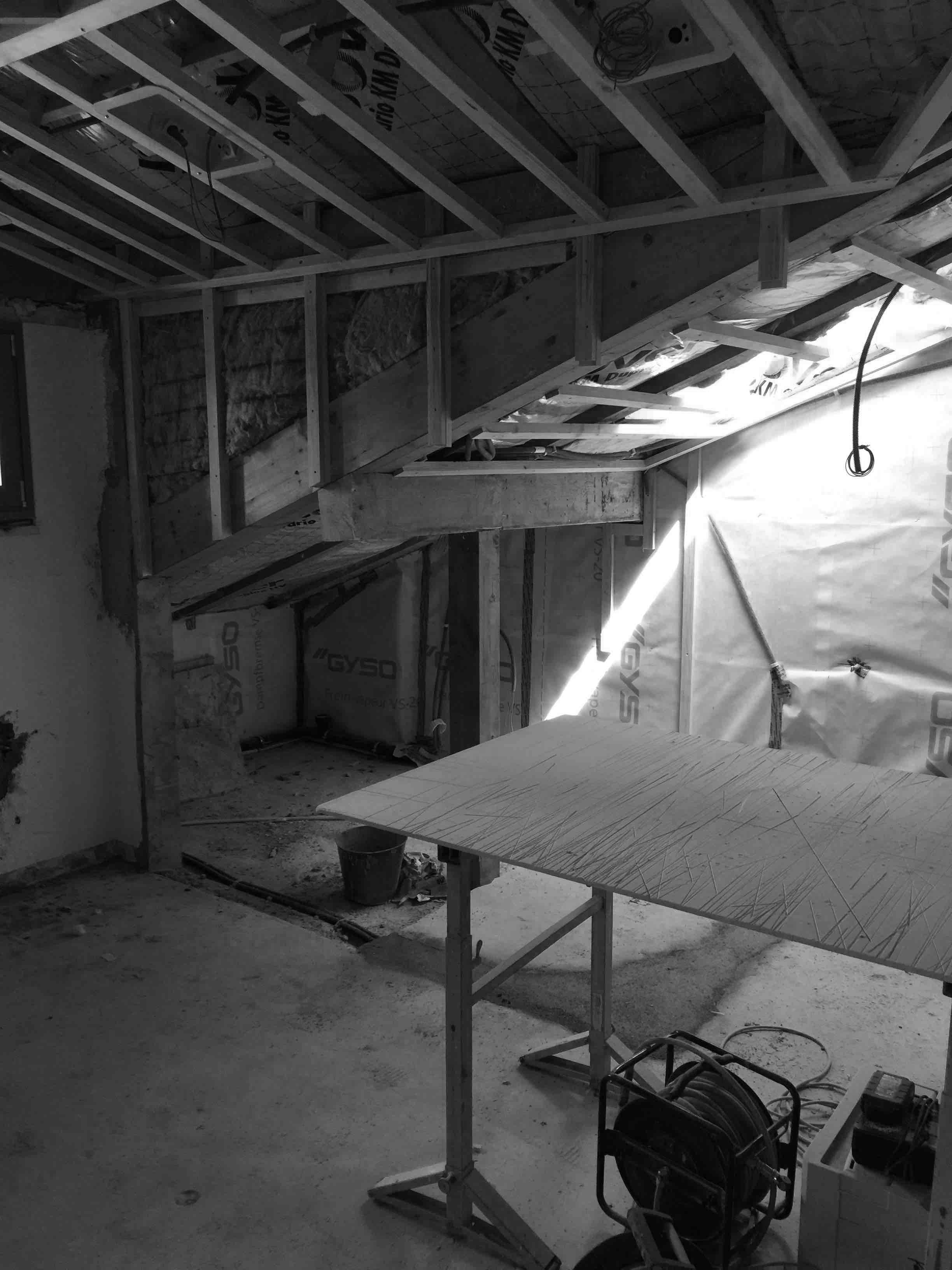 A partially constructed room featuring exposed wooden beams, a work table, and a light beam illuminating the space.