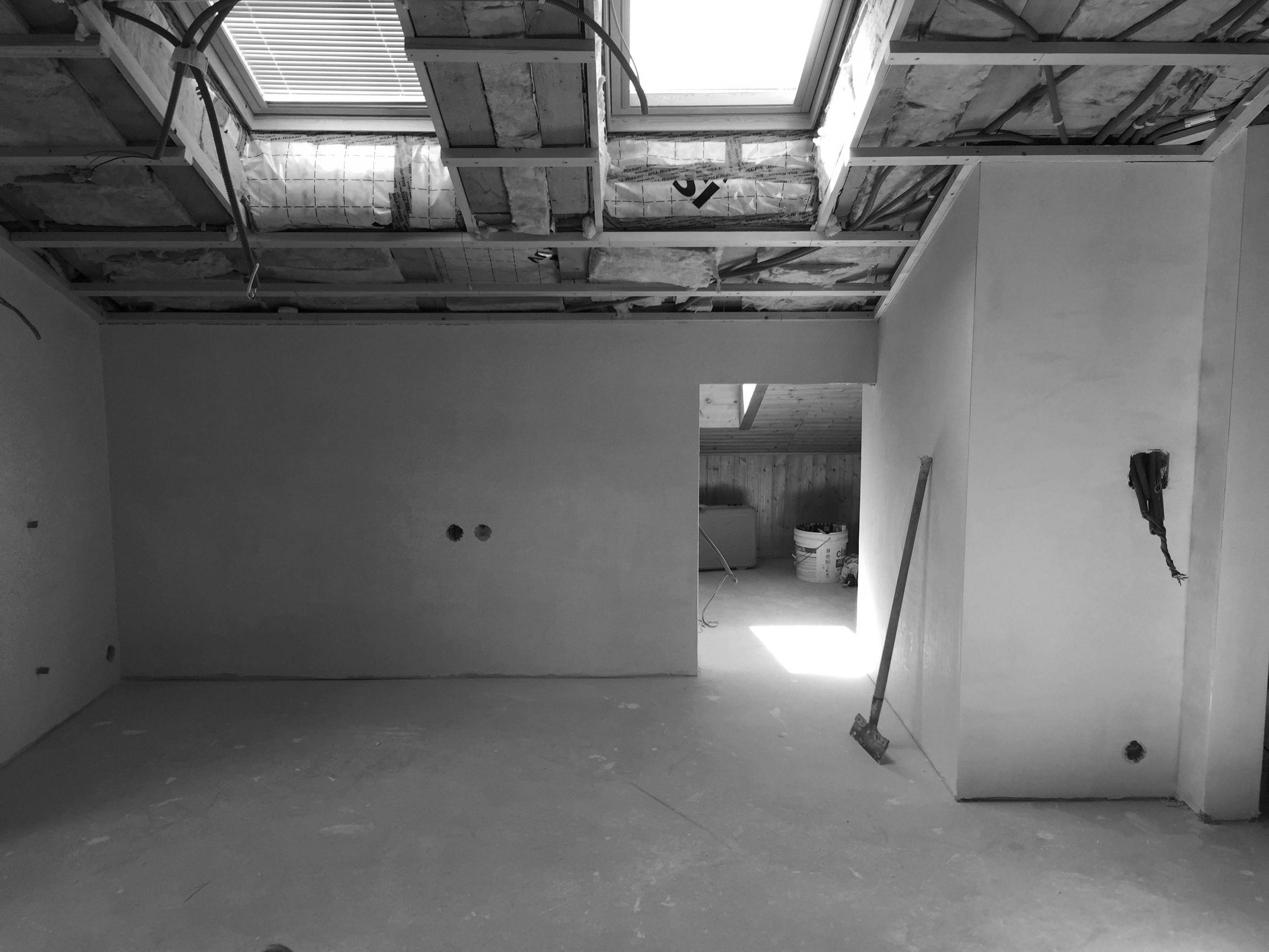 A partially finished room with smooth, white walls, exposed ceiling structure, and a skylight, featuring construction tools.